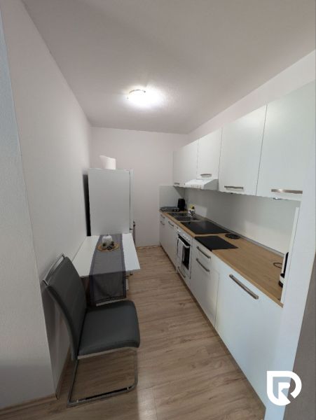 A kitchen in a 2-room apartment with a wooden decor floor and white cabinets.