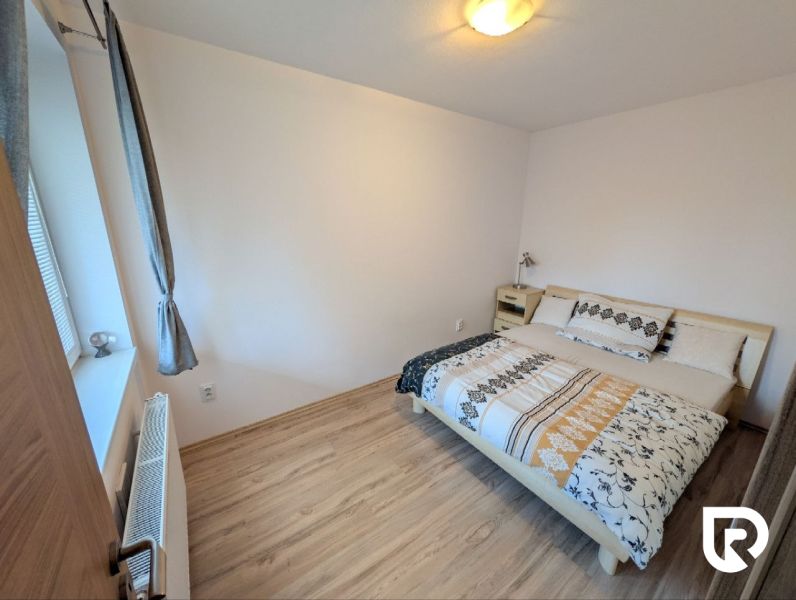 A bedroom with a wood-patterned floor in a two-room apartment, bed by a white wall.