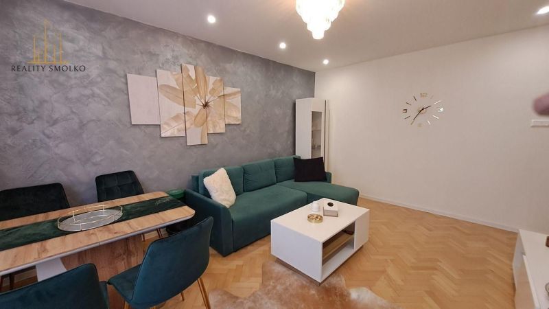 A living room in a two-room apartment with a wooden decor floor and a green sofa.
