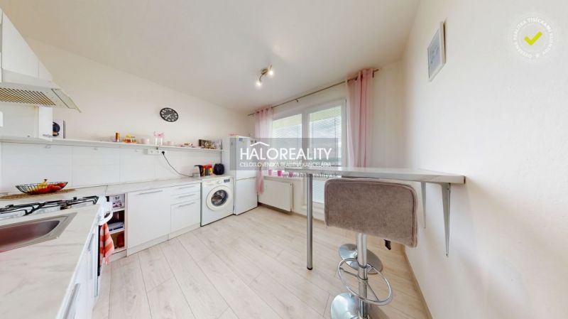 The kitchen of a two-room apartment with a wooden decor floor, white furniture, and a bar counter.