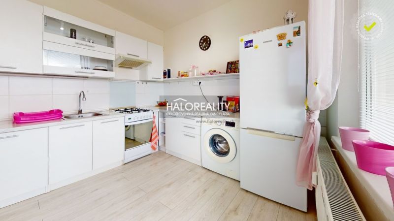 A kitchen in a 2-room apartment with white cabinets and a washing machine. Floor with wood decor.