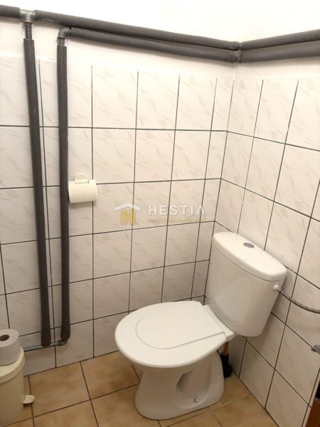 A restroom in commercial premises with white tiles and a floor with a subtle pattern.