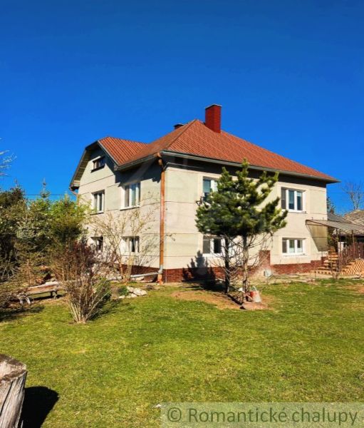 A family house in Nové Hony with a red roof, surrounded by a garden with coniferous trees.