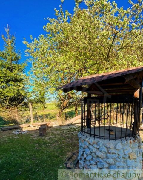 A well in the garden of a family house in Nové Hony surrounded by trees and a grassy plot.