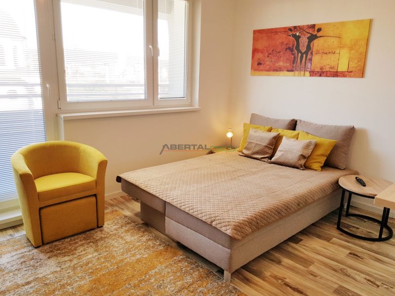 A one-room apartment with a bed, a yellow armchair, and a floor with a wooden decor.