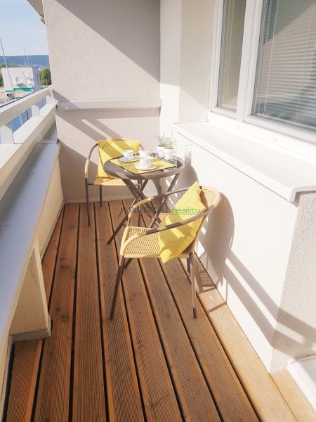 A balcony with a wooden decor floor, chairs, and a table in a studio apartment.