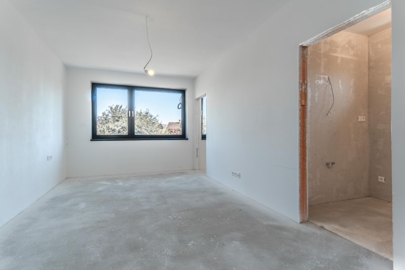 An empty room with a large window in a family house, concrete floor, and incomplete walls.