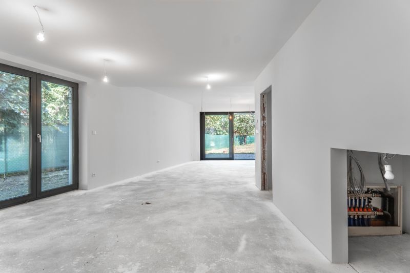 A spacious room with light walls, concrete flooring, and large windows in a family house.