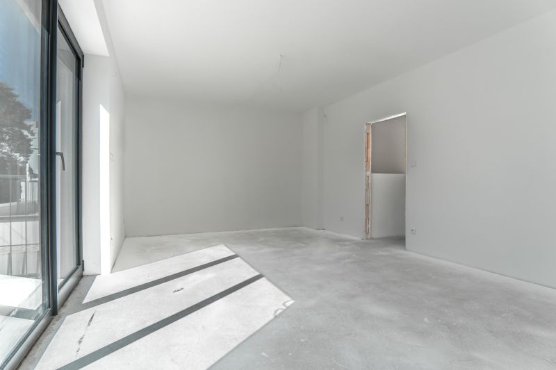 A spacious room with large windows, white walls, and a raw floor. Family house.