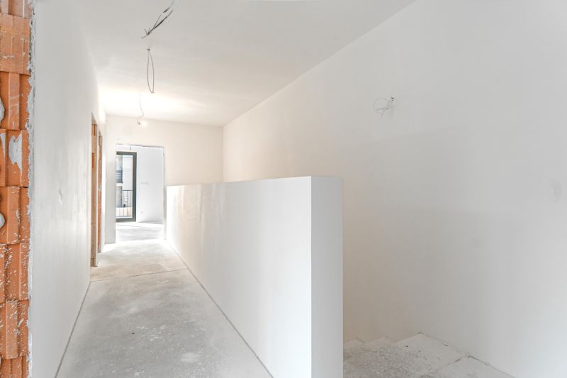 A hallway in a family house with white walls and a bare concrete floor surface.