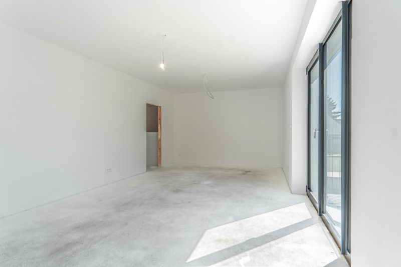 A spacious room with white walls and a large window in a family house.