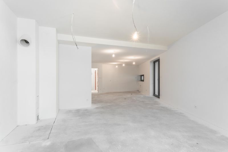 A spacious unfurnished interior of a family house with white walls and a raw floor.