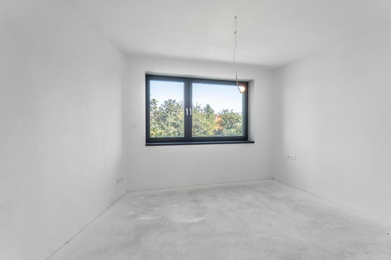 A minimalist room with a large window in a family house, white walls, and a concrete floor.