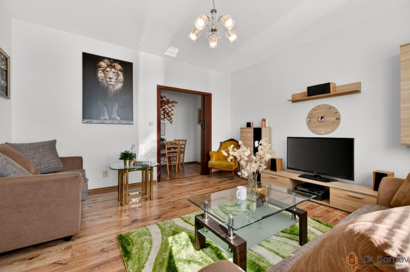 Living room in a two-room apartment with a sofa, an armchair, a television, and a floor with a wooden decor.