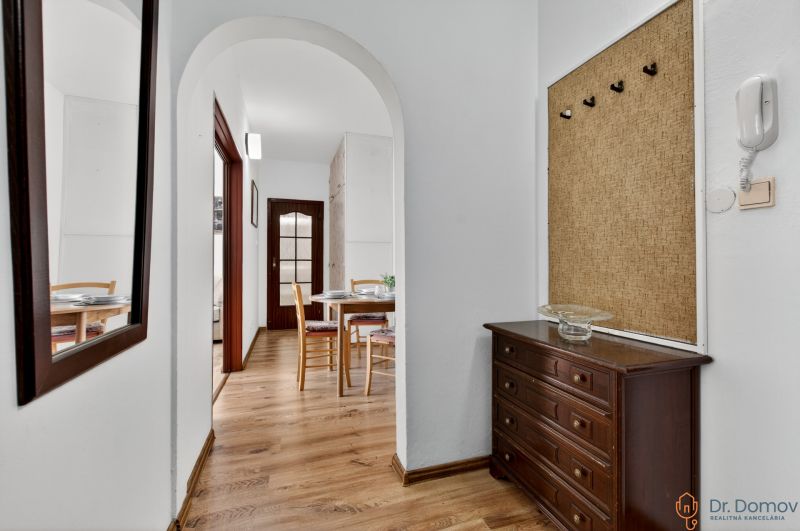 A hallway in a 2-room apartment with a wooden decor floor, a mirror, and a table in the background.