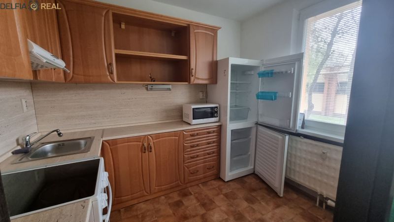 A kitchen in a studio apartment with wooden cabinets, a microwave, and an open refrigerator.