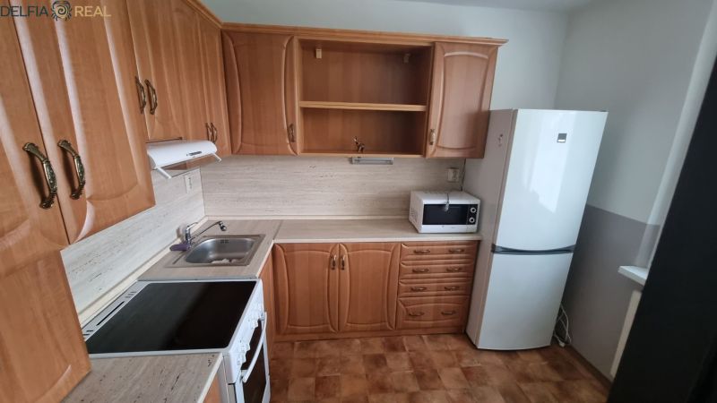 A kitchen in a one-room apartment with wooden cabinets, a microwave, and a white refrigerator.