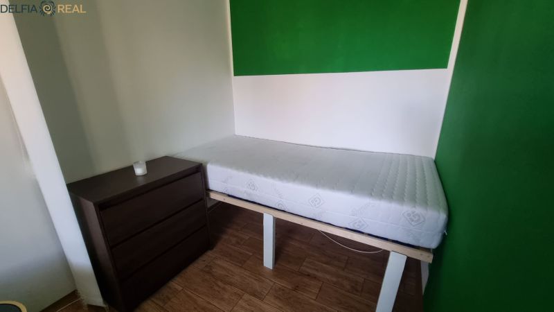 Simple furnishing of a studio apartment with a bed and a chest of drawers on a floor with a wooden decor.