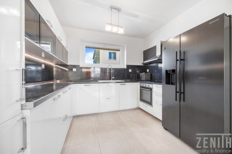 A kitchen in a family house with built-in appliances and glossy white cabinets.