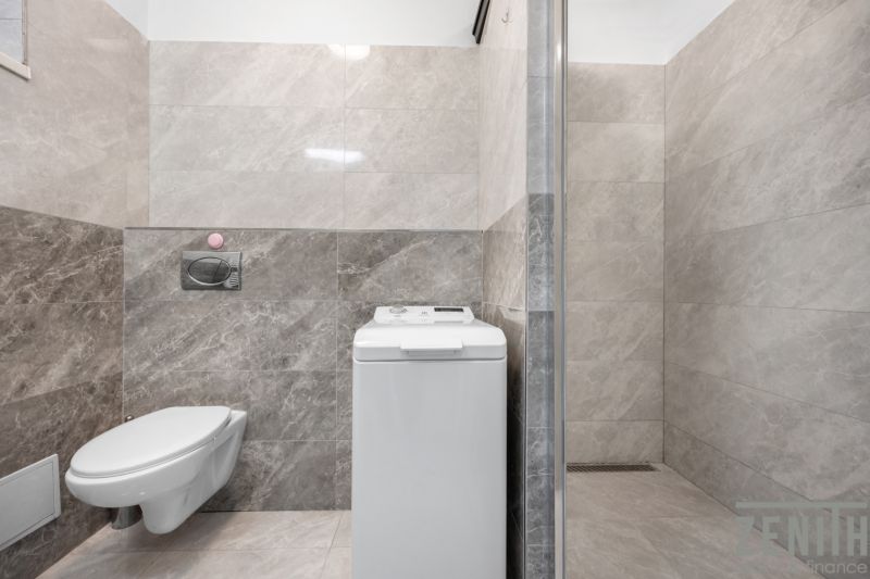 A bathroom in a family house with a washing machine and a shower, tiled with marble tiles.
