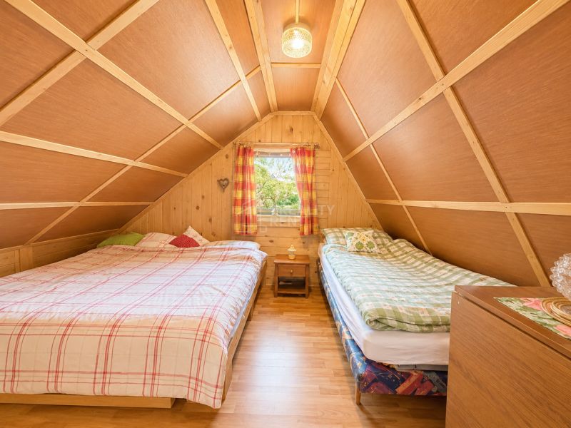 Attic bedroom with two beds, wooden decor, and a window in a cabin.