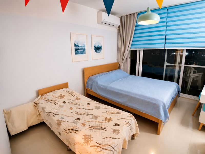 A bedroom in a one-room apartment with two beds and colorful blinds.