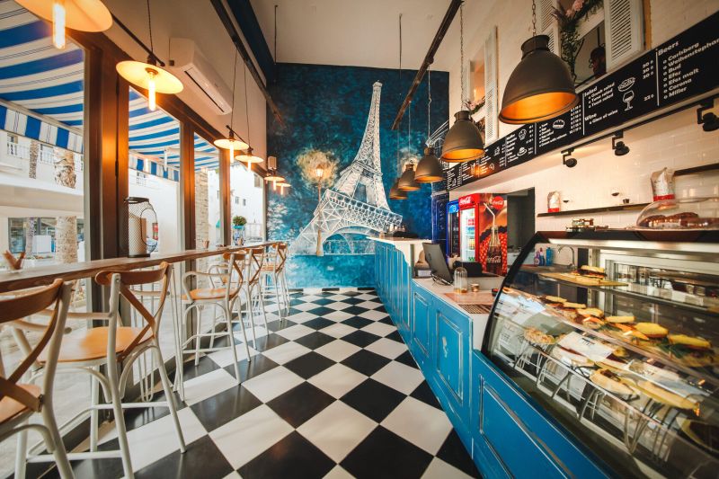 A café with a black and white floor, the Eiffel Tower on the wall, bright lights, wooden chairs.