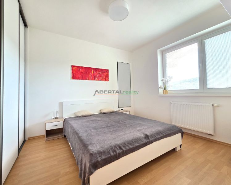A bedroom in a two-room apartment with a wooden decor floor and minimalist furniture.