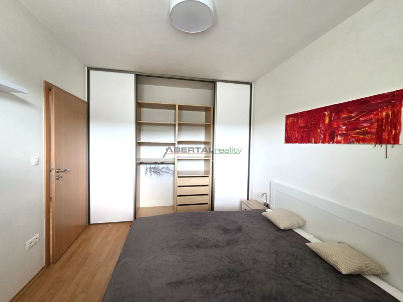 A bedroom in a 2-room apartment with a wooden decor floor, a built-in wardrobe, and an abstract painting.