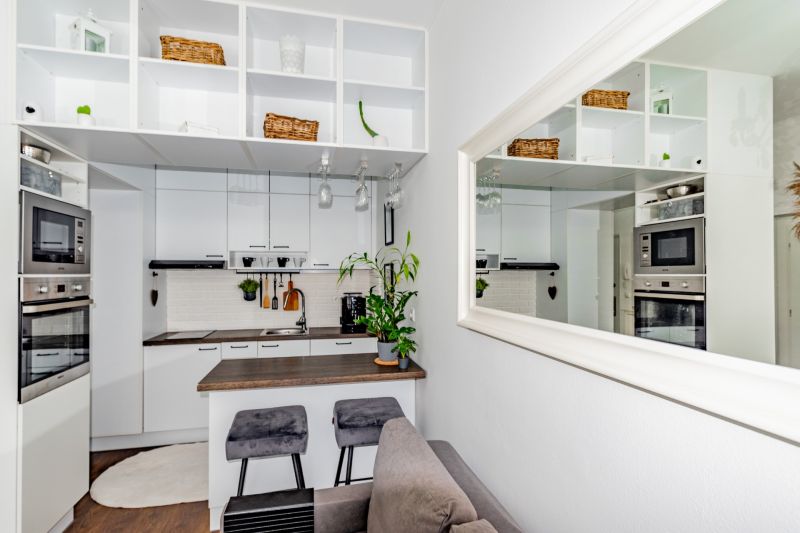 The kitchen in a 2-room apartment with white cabinets and a mirror, wood-effect flooring.