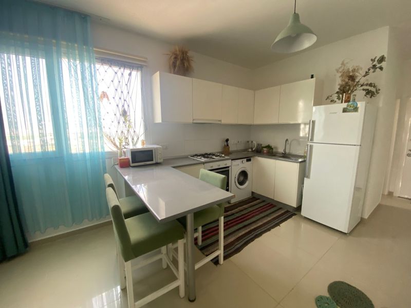 A one-room apartment kitchen with a window, appliances, and light-colored furniture.