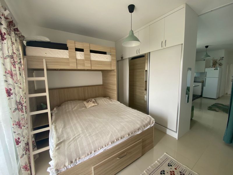 A space in a studio apartment with a bunk bed, built-in wardrobe, and floral curtains.