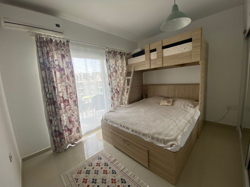 A bedroom in a studio apartment with a bunk bed, curtains, and a balcony.