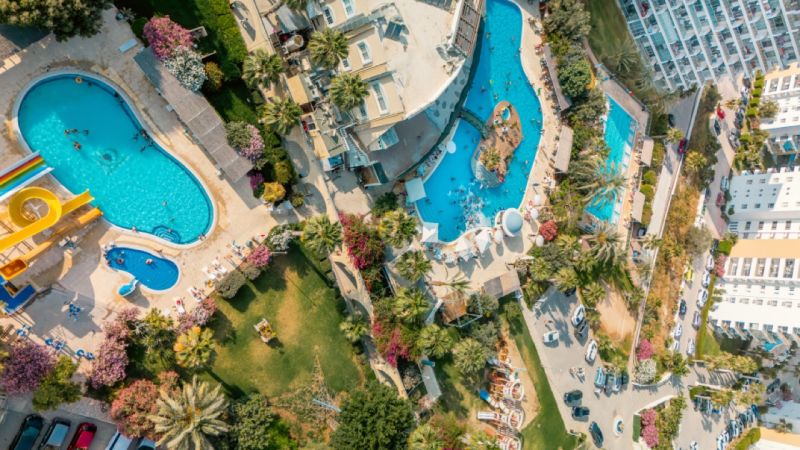 Aerial view of pools and gardens in the city of Iskele, surrounded by greenery and buildings.