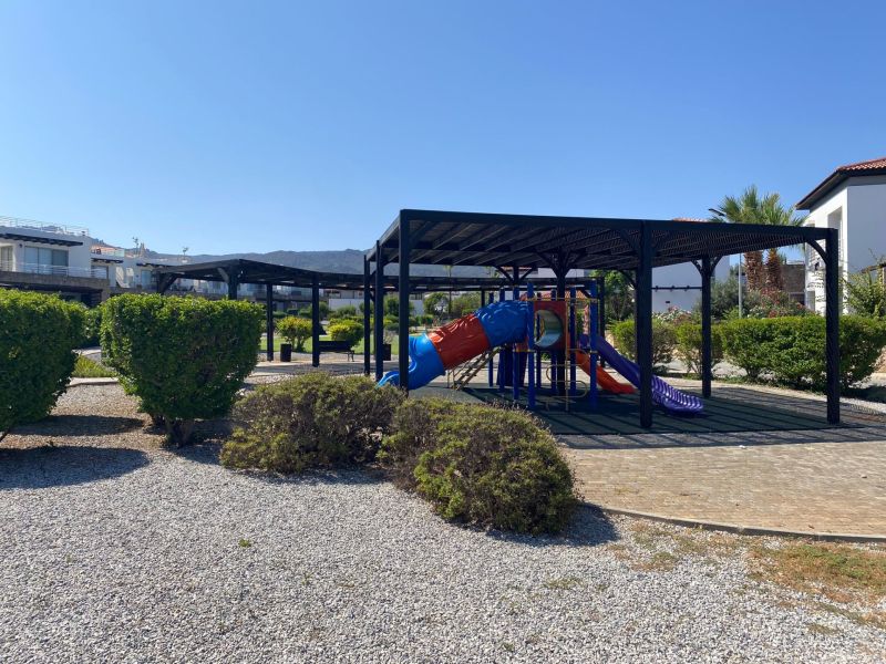 A children's playground in Tatlisu surrounded by greenery and walkways near 2-bedroom apartments.