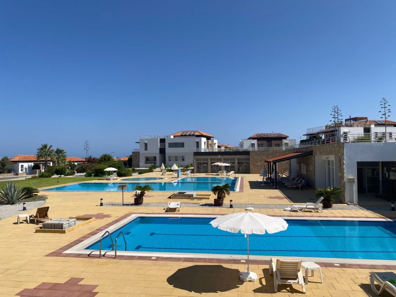 Exterior of the complex in Tatlisu with pools and sunbeds, ideal for a 2-bedroom apartment.