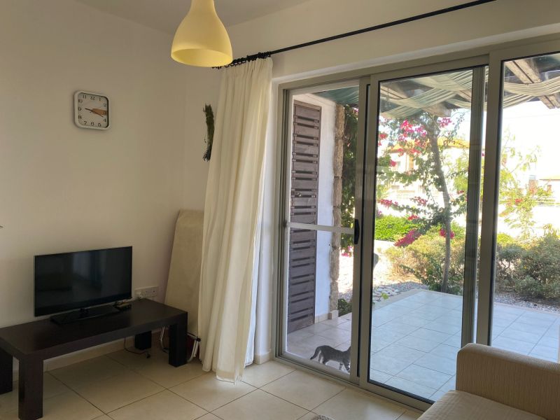 Living room of a two-room apartment with a television, curtains, and sliding doors to the terrace.