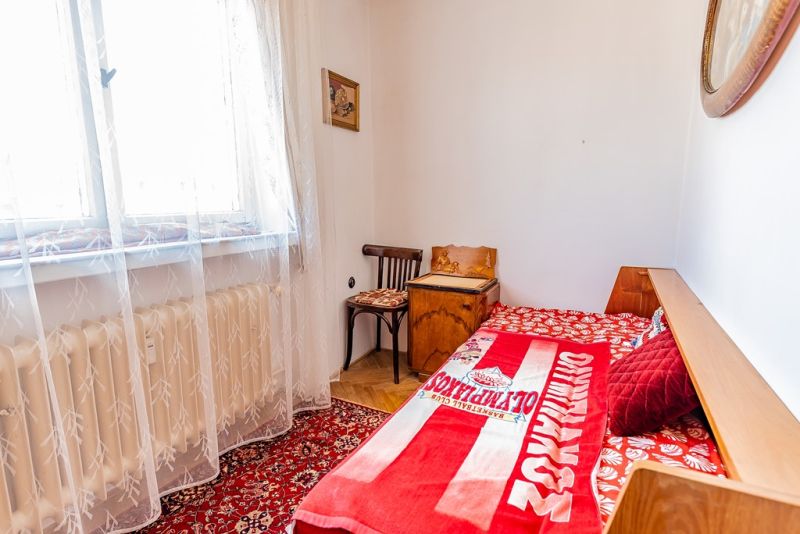 Simple bedroom with a bed, red carpet, chair, and wood-patterned floor.