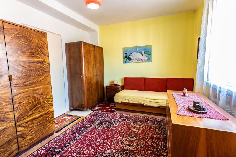 A room in a two-room apartment with wooden furniture and a red carpet.