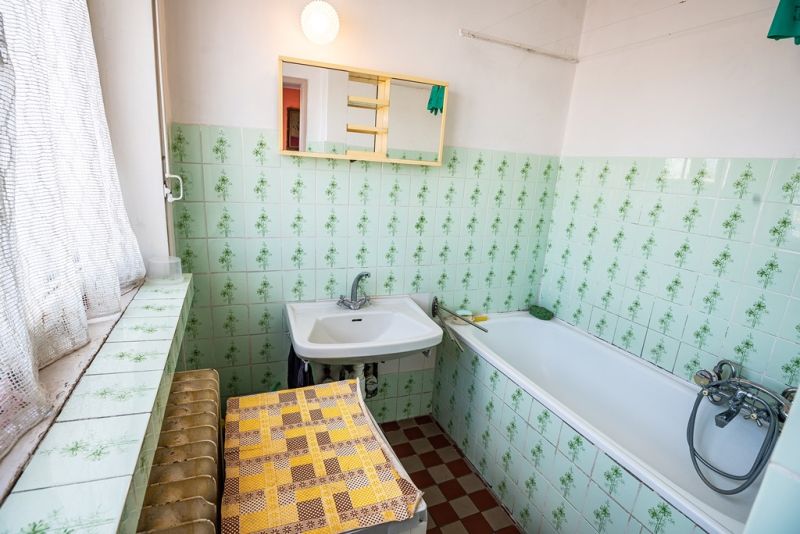 A bathroom with green tiles and a bathtub in a 2-room apartment.
