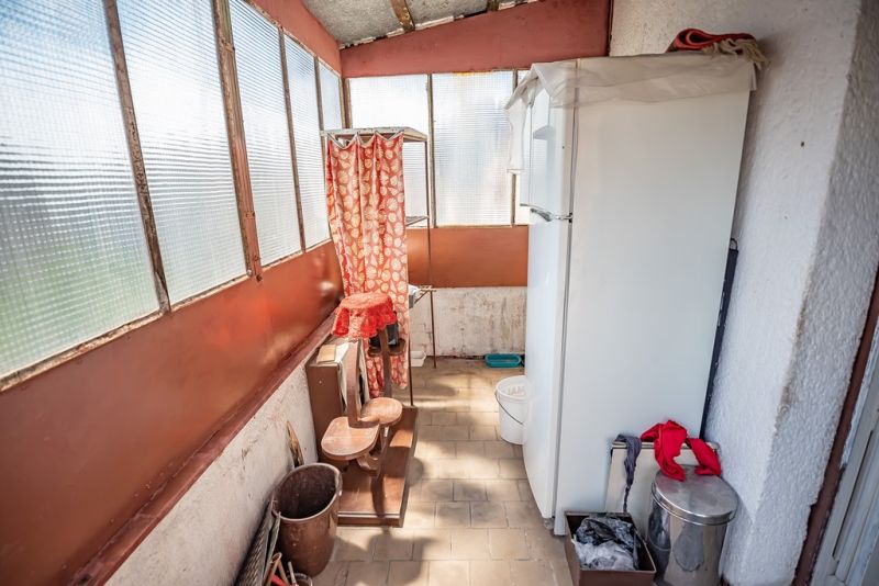 A balcony with a refrigerator, flower pots, and plastic windows in a 2-room apartment.