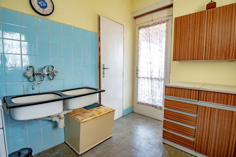 A kitchen in a 2-room apartment with blue tiles and wooden decor furniture.