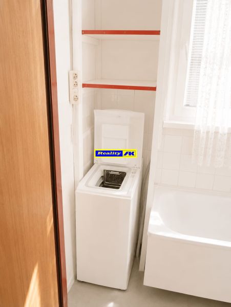 Bathroom in a 3-room apartment with a washing machine, bathtub, and shelves.