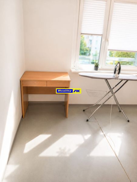 A bright room in a 3-room apartment with a desk, ironing board, and window.