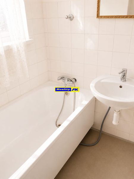 A bathroom with a bathtub and a sink in a 3-room apartment. Light tiles on the walls.