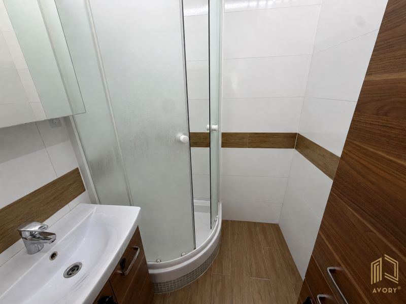 A bathroom with a shower and a floor with a wooden decor in a 2-room apartment.