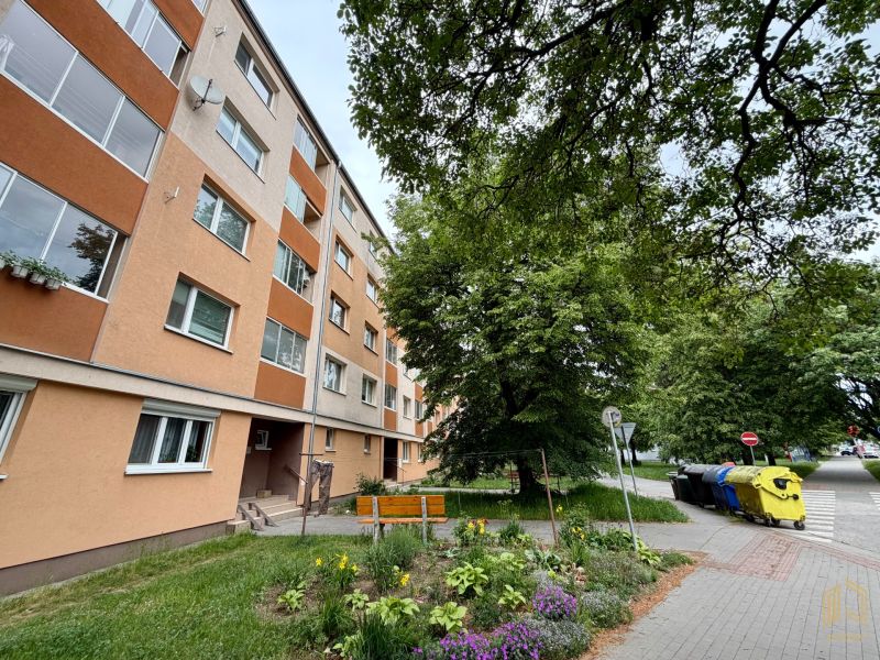 Exterior of a 2-room apartment on Palárikova Street in Senica, with nearby greenery and a park bench.
