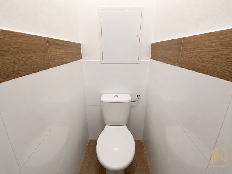 A toilet in a 2-room apartment with wood and white decor tiles.