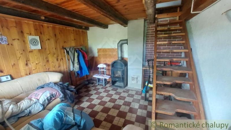 The interior of the cabin with wooden paneling, a stove, and a wooden staircase.