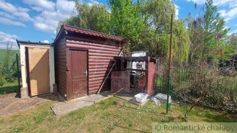 A wooden cottage in Holíč surrounded by greenery and a fence under a blue sky.